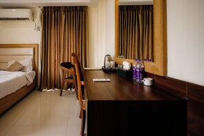 Quarto de hotel com cama, uma cadeira de madeira, escrivaninha com controle remoto, chaleira e espelho.