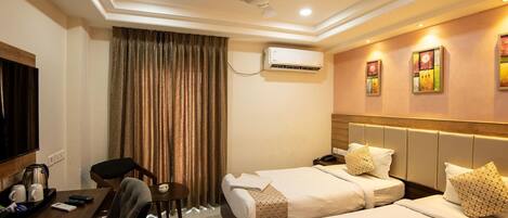 A hotel room with two beds, a desk with a chair, a television, and an air conditioning unit.