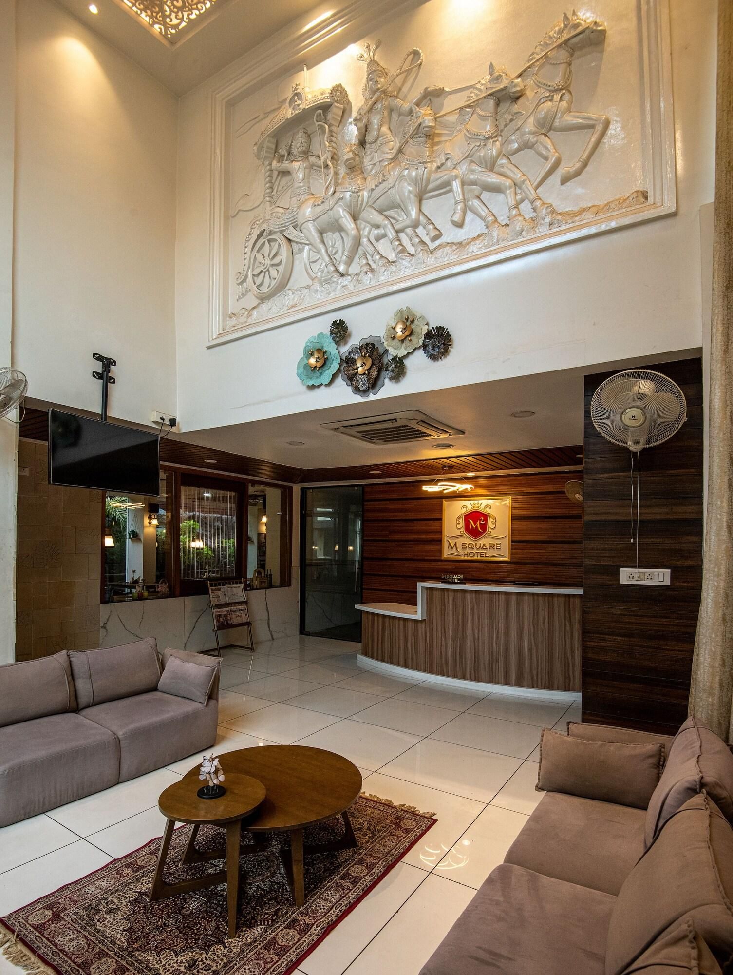 Un hall de hotel con mostrador de recepción, sofás, una mesa de centro y un mural decorativo en el techo.