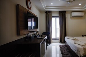 A hotel room with a bed, a desk with a television, a coffee maker, and an air conditioning unit. - M Square Hotel-hitec City (Hyderabad)