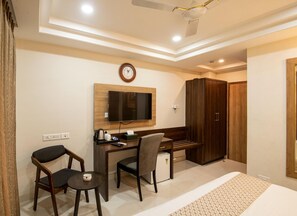 A hotel room with a desk, two chairs, a television, a wardrobe, and a bed.