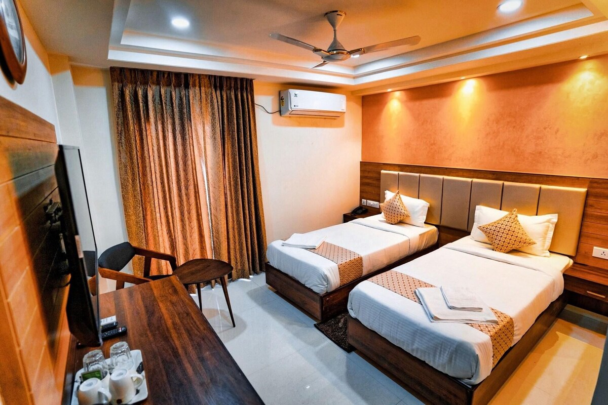 A hotel room with two beds, a desk with a chair, a TV, and an air conditioning unit.