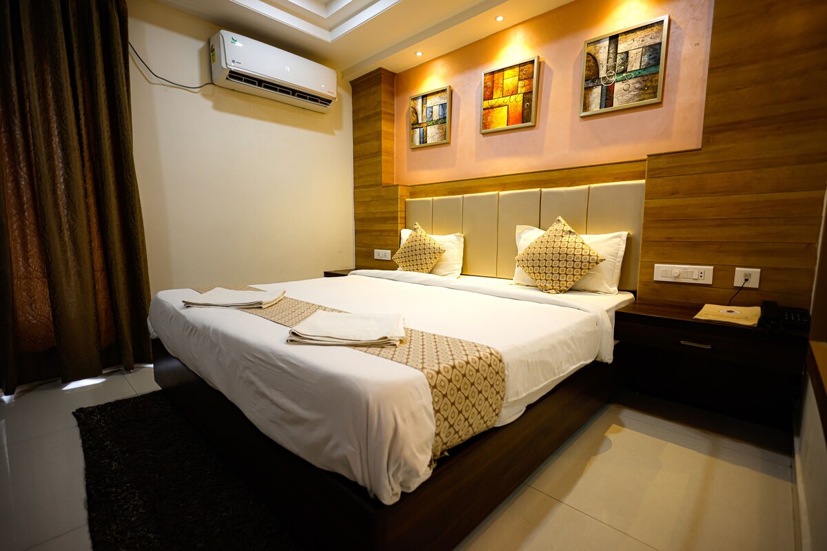 A modern hotel room with a large bed, a bedside table, an air conditioning unit, and artwork on the wall.