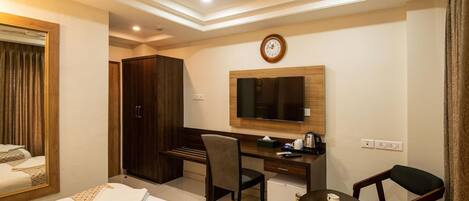 A hotel room with two beds, a desk, a chair, a small table, a television, and a clock on the wall.