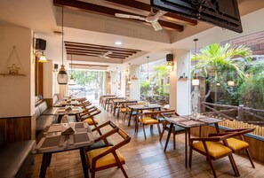 A restaurant with wooden tables and chairs, a high ceiling with exposed beams, and a view of greenery outside.