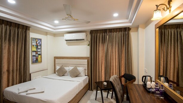 A hotel room with a bed, a desk with a chair, a mirror, an air conditioning unit, and a ceiling fan.