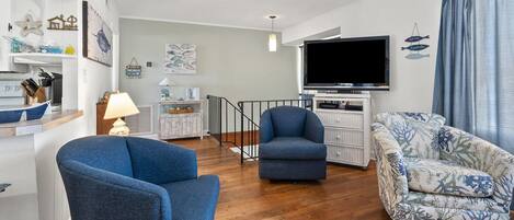A modern living room with a flat-screen TV, two sofas, a small table, and a staircase.