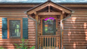 Een houten chalet met een veranda, een raam met luiken en een bloemenmand.