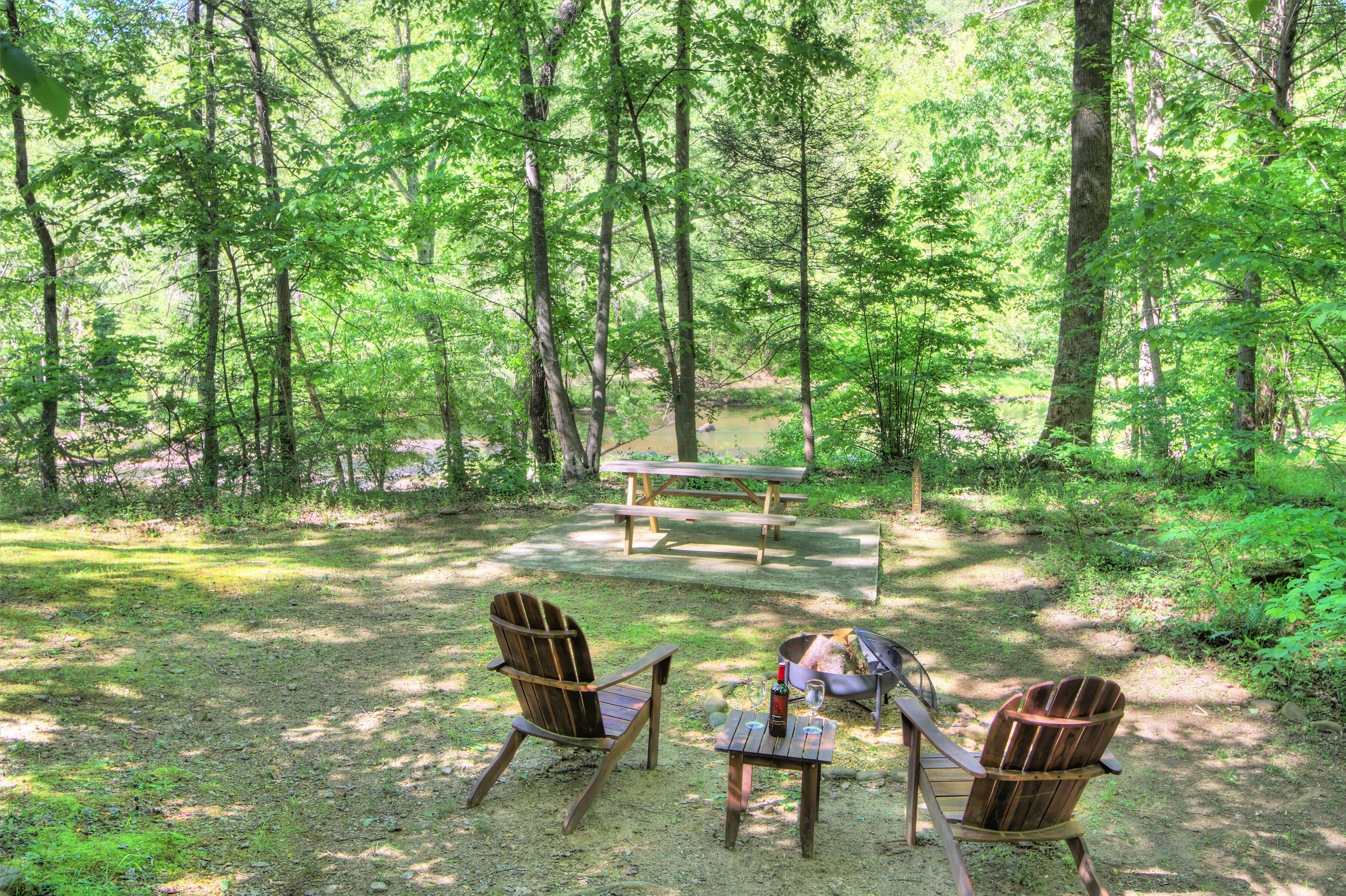 Un terrain de camping boisé équipé de tables de pique-nique, de deux chaises Adirondack et d’un barbecue.