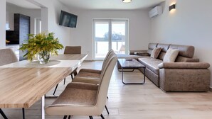 A modern living room with a wooden dining table, beige sofas, and a large window. - Villa Galici by Interhome (Umag/Murine)