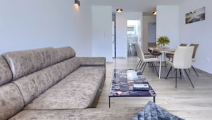 A modern living room with a sofa, a coffee table with a magazine, and a dining area with chairs and a table. - Villa Galici by Interhome (Umag/Murine)