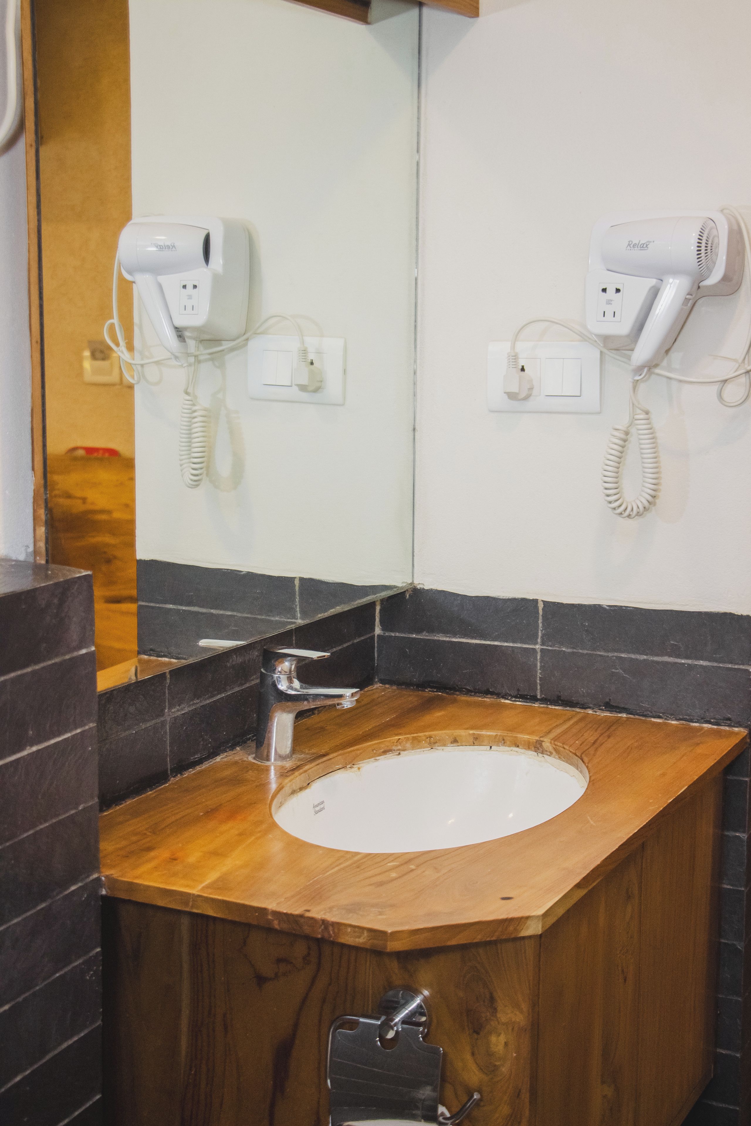 A bathroom with a wooden vanity, a white sink, and two hair dryers mounted on the wall.