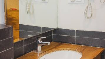 A bathroom with a wooden vanity, a white sink, and two hair dryers mounted on the wall.