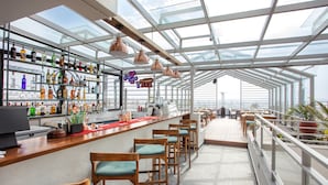 A modern bar with a glass ceiling, wooden bar stools, and a variety of liquor bottles. - Hotel Bhrikuti Tara (Kathmandu)
