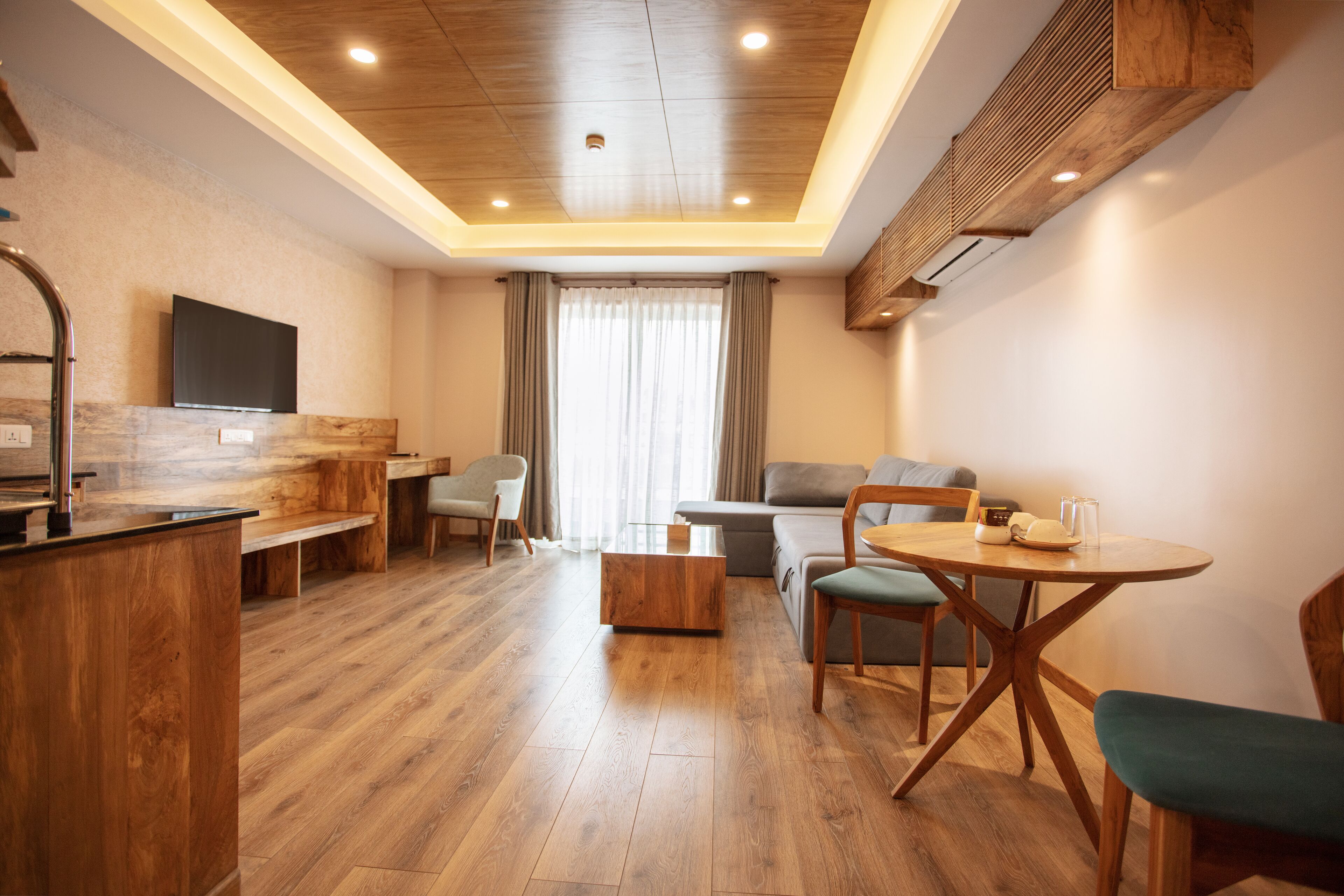 Una sala de estar moderna con piso de madera, un sofá, una mesa de comedor con sillas y un televisor montado en la pared.