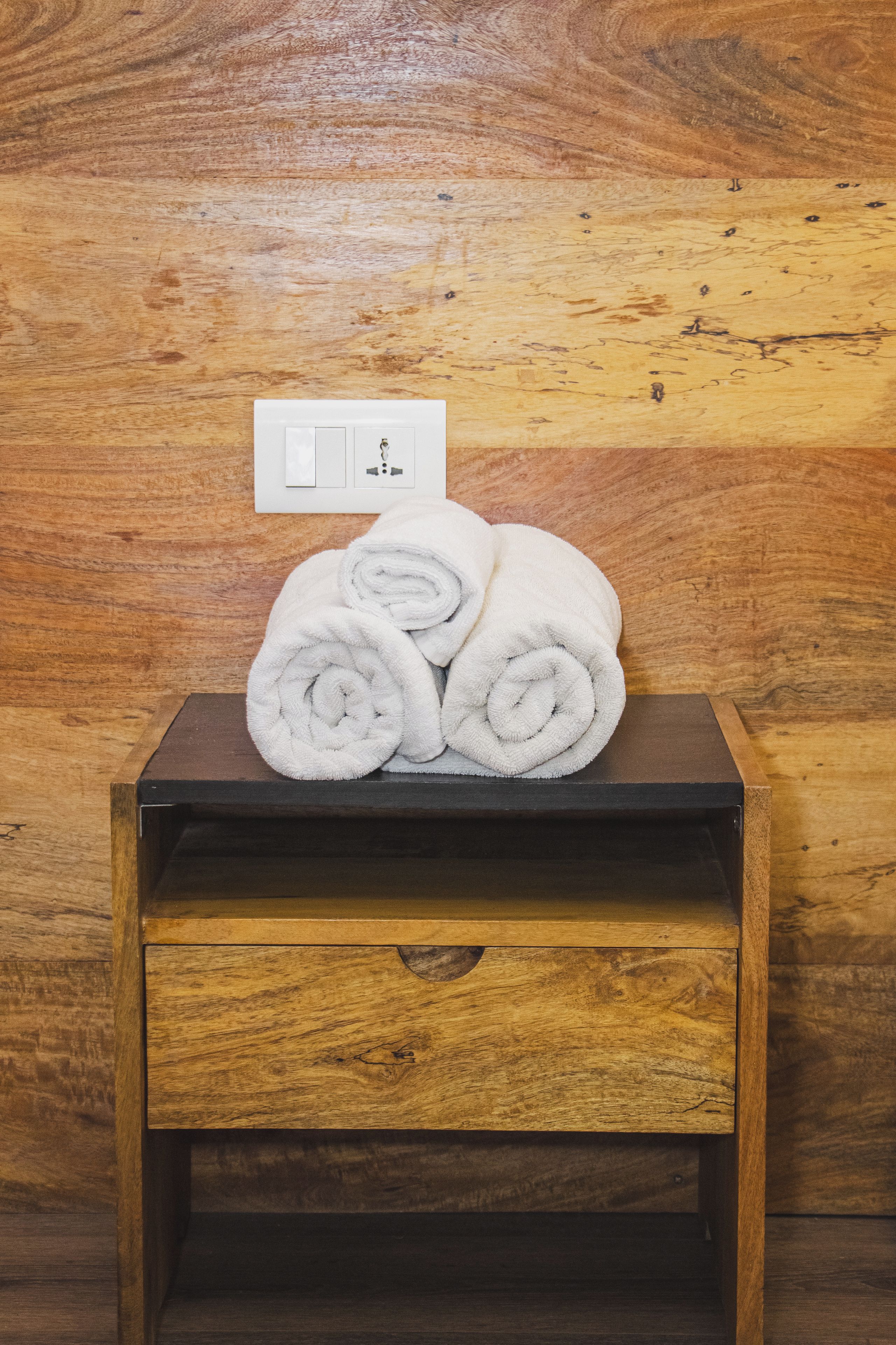 A wooden bedside table with a white towel rolled up on top.