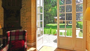 A room with a stone wall, a plaid chair, a white door leading to a garden, and a lamp. - Beautiful home in Groléjac with WiFi (Groléjac)