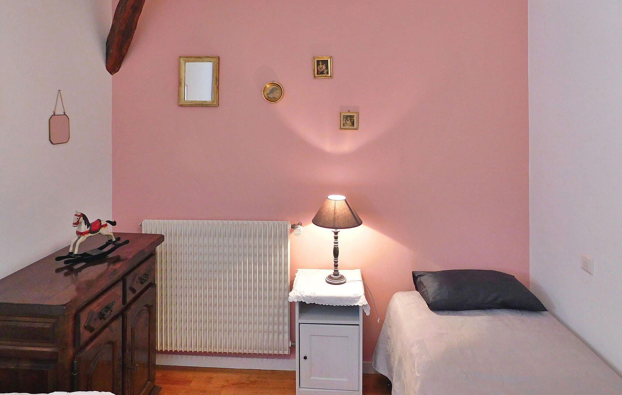 Une chambre avec une commode en bois, un radiateur, un lit avec un oreiller noir et une lampe sur une table de chevet.