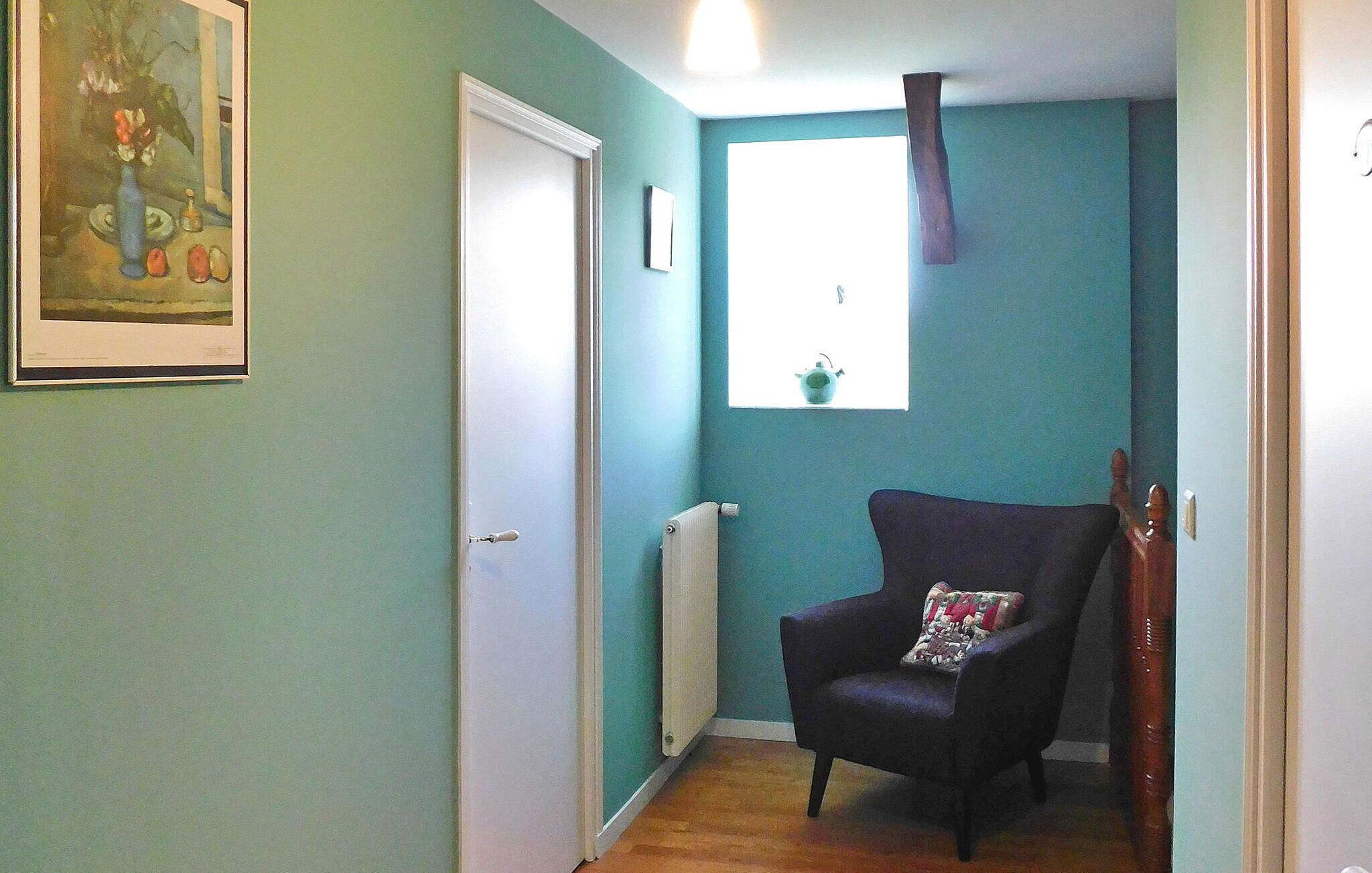 Ein Korridor mit türkisfarbenen Wänden, einem schwarzen Stuhl mit Sitzkissen, einem Heizkörper und einem gerahmten Gemälde an der Wand.
