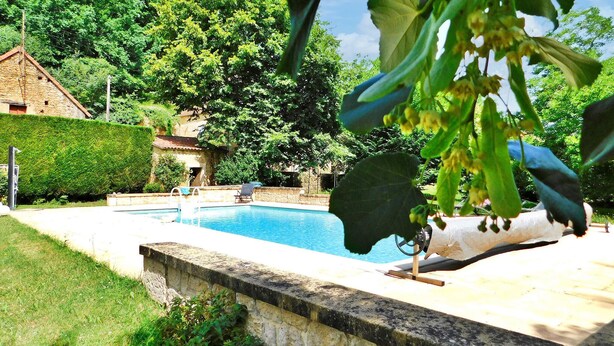 A swimming pool with a stone wall, a lounge chair, and a building in the background. - Beautiful home in Groléjac with WiFi (Groléjac)