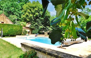 Une piscine bordée d’un mur en pierre, une chaise longue et un bâtiment en arrière-plan.