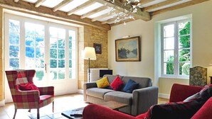 A living room with a sofa, armchairs, and a coffee table. There are large windows with a view of greenery outside. - Beautiful home in Groléjac with WiFi (Groléjac)