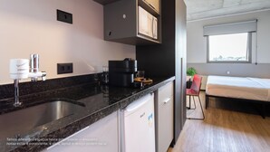 Una cocina moderna con microondas integrado, cafetera y un lavabo. Hay un refrigerador pequeño y una ventana con vista a la ciudad.