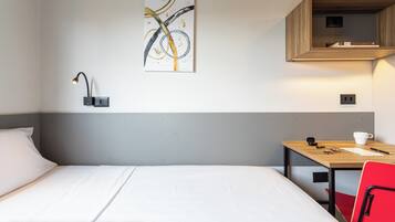 Habitación de hotel con cama, escritorio, silla, una obra de arte en la pared y estante con libros.