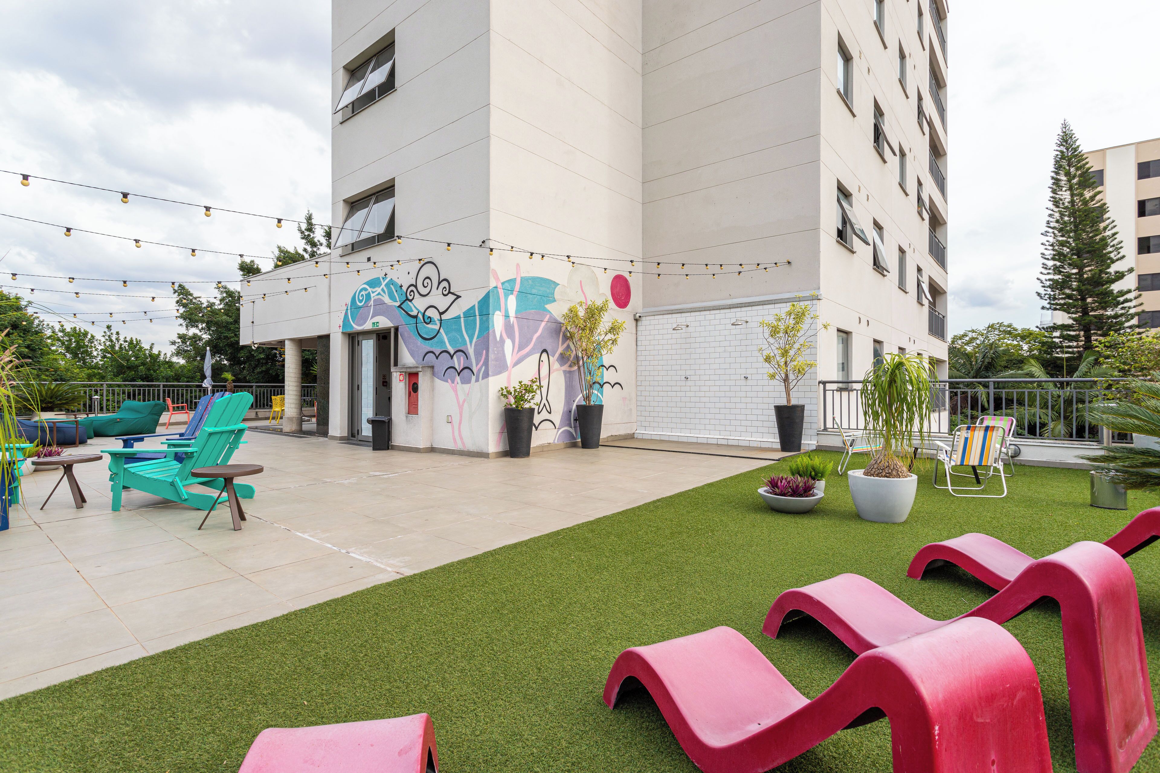 An outdoor area with artificial grass, red and teal lounge chairs, and potted plants.