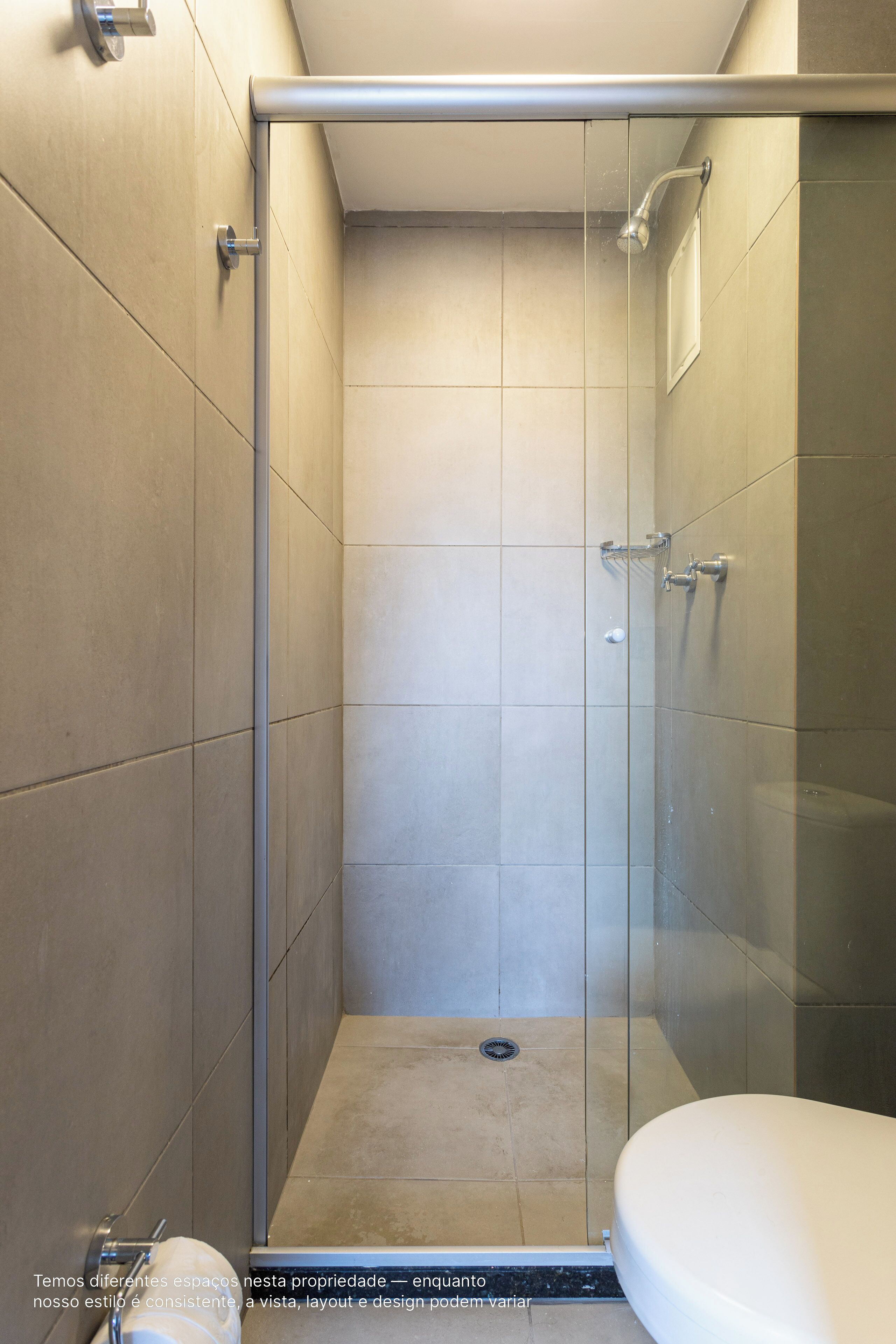 Une douche fermée par des parois de verre, avec des toilettes blanches visibles sur la droite.