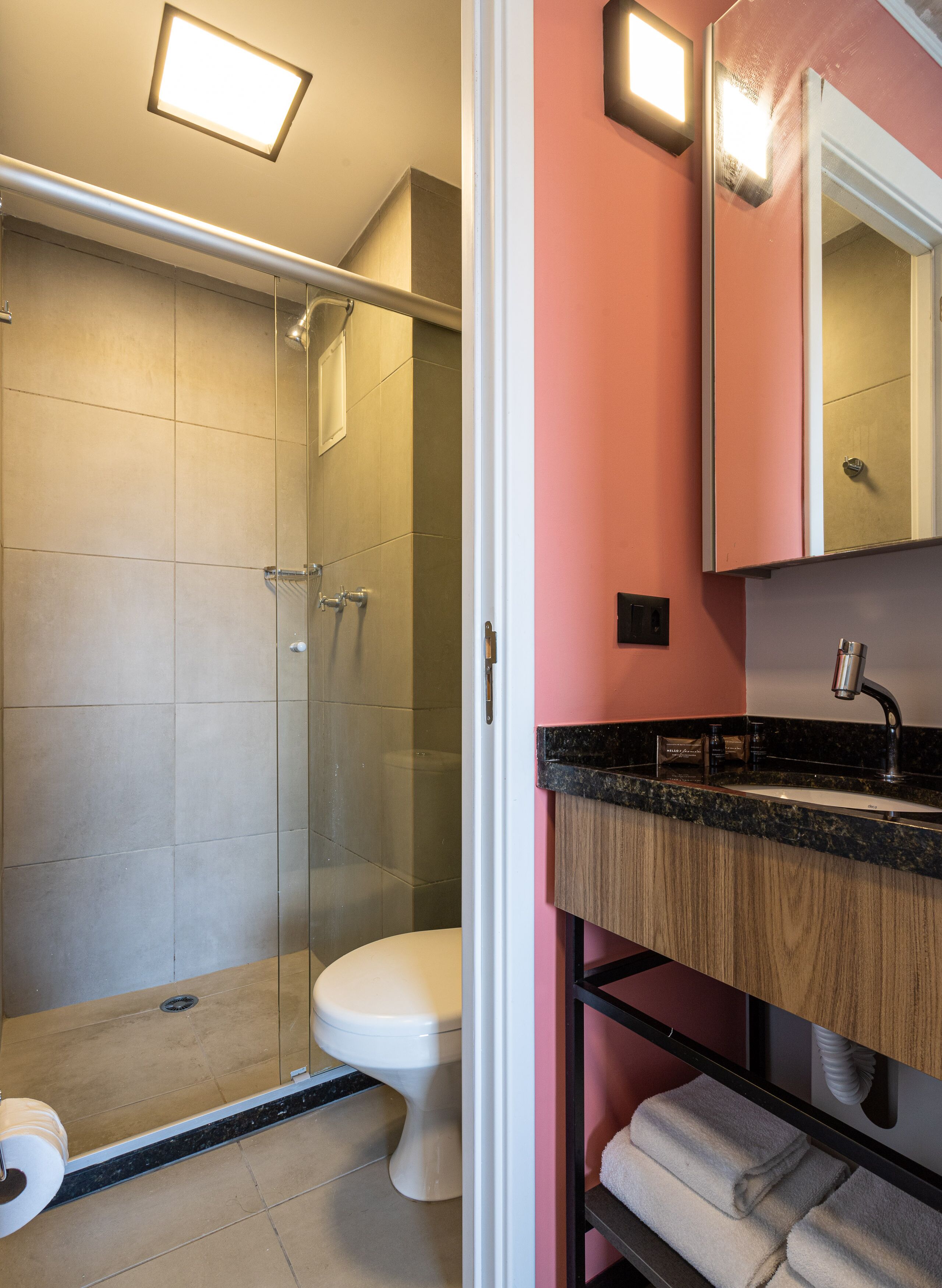 Een moderne badkamer met een douchecabine van glas, een wit toilet, een wastafel met een zwart aanrechtblad en een spiegel boven de wastafel.