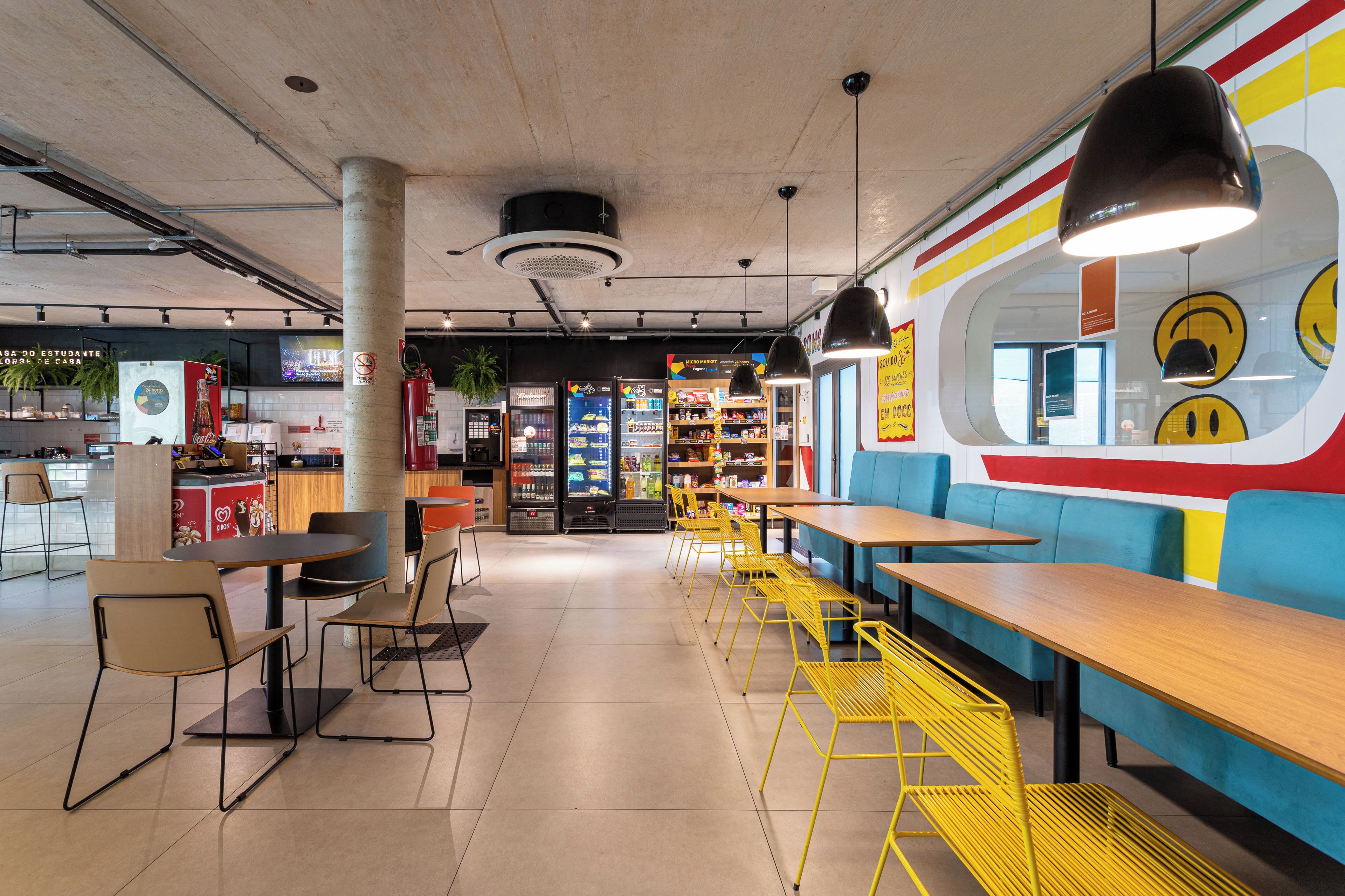 A modern cafe with yellow chairs, wooden tables, and a colorful wall mural.