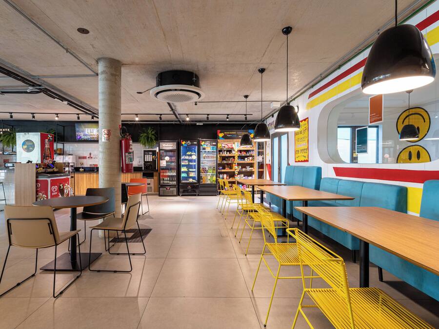 A modern cafe with yellow chairs, wooden tables, and a colorful wall mural.