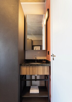 A modern bathroom with a wooden vanity, a built-in sink, and a mirror above it. - Caza Noz by Viva - Apartamentos novos, com ótima estrutura e área comum próximo à USP e Butantã (São Paulo)