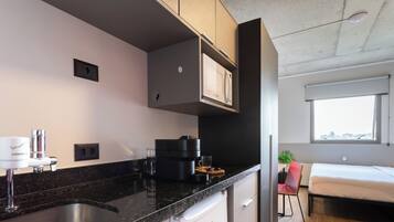 A modern kitchen with a built-in microwave, a coffee machine, and a sink. There is a small refrigerator and a window with a view of the city.