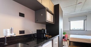 Une cuisine moderne équipée d’un four à micro-ondes encastré, d’une machine à café et d’un évier. On y trouve également un petit réfrigérateur et une fenêtre donnant sur la ville.