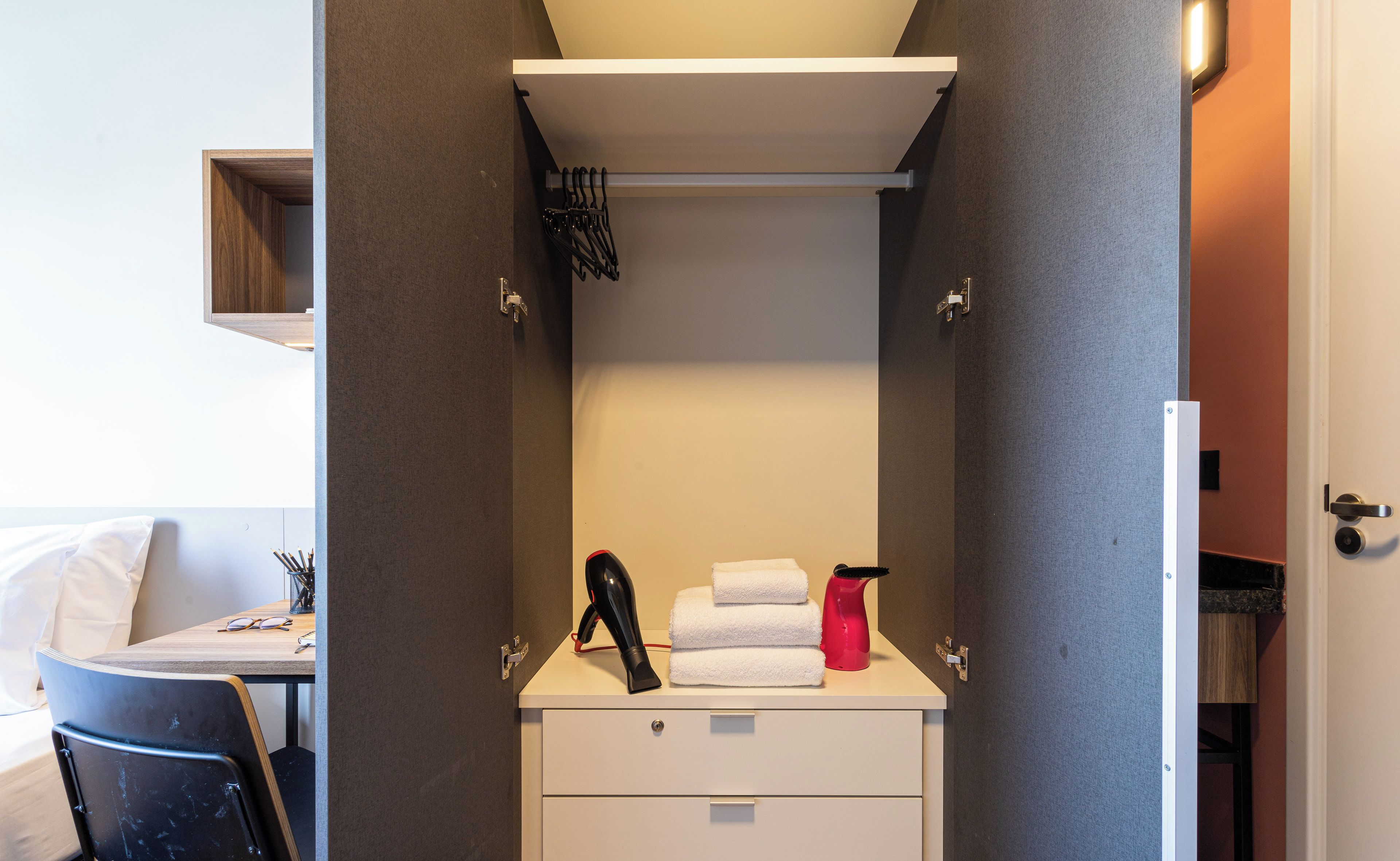 A compact bathroom with a towel rack, a hairdryer, and a red spray bottle on the counter.