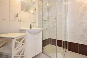 A modern bathroom with a glass-enclosed shower, a white sink, and a mirror.