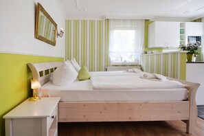 A hotel room with a bed, bedside table, lamp, and a view of the kitchen area. - An den Linden - Gemütliche Ferienwohnung in Zentrum von Heringsdorf mit Terrasse und Wlan (Heringsdorf)
