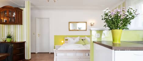 A hotel room with a bed, a desk, a chair, a chandelier, a mirror, and a potted plant.