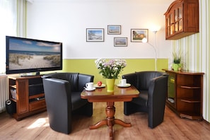 Ein Zimmer mit Fernseher, zwei schwarzen Ledersofas, einem Holztisch mit Blumenvase und einem Schrank.