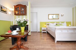 A hotel room with a bed, bedside table, lamp, and a desk with a chair and a vase of flowers.