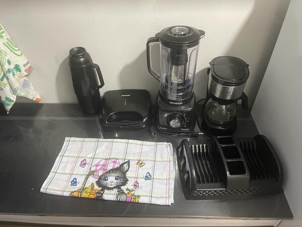 A kitchen counter with a blender, coffee maker, and a cloth with a cat design.