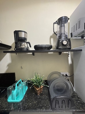 A kitchen counter with a coffee maker, a blender, a small plant, and a dish rack. - Apartamento na Praia do Forte 😉 , Centro Cabo Frio - RJ 118 (Centro Cabo Frio)
