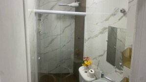 A modern bathroom with a glass shower enclosure, a white pedestal sink, and a mirror with a gold frame. - Apartamento na Praia do Forte 😉 , Centro Cabo Frio - RJ 118 (Centro Cabo Frio)