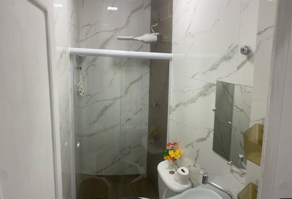 A modern bathroom with a glass shower enclosure, a white pedestal sink, and a mirror with a gold frame. - Apartamento na Praia do Forte 😉 , Centro Cabo Frio - RJ 118 (Centro Cabo Frio)