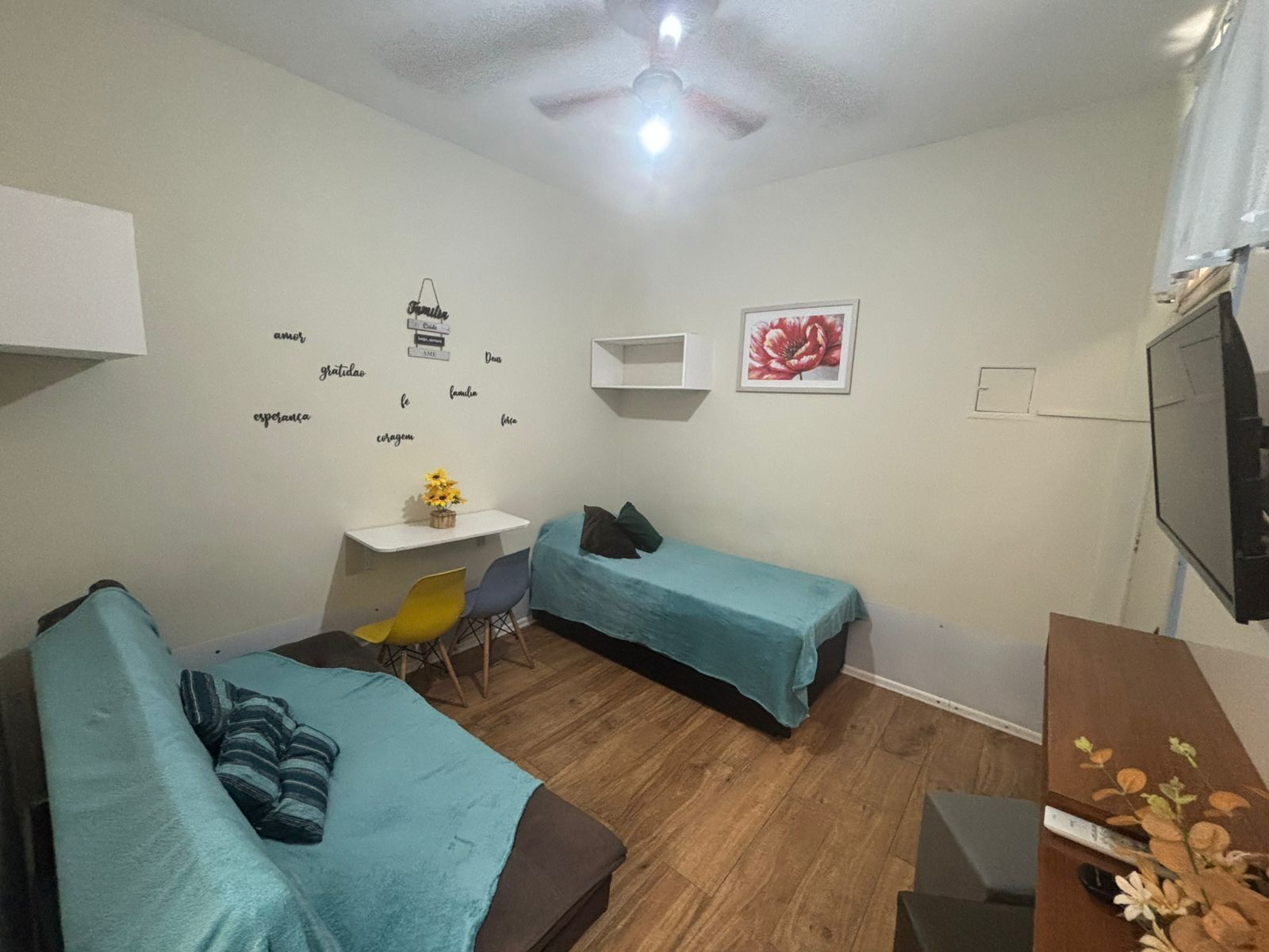 Een kleine, goed verlichte kamer met twee enkele bedden, een bureau met stoel en een televisie.