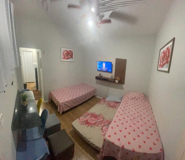 Huoneessa on kaksi erillistä sänkyä, pieni työpöytä, televisio ja kattotuuletin.