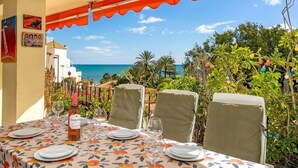 A table set for dining with a view of the sea, covered by a red awning, and surrounded by greenery. - Fuengirola Seaside Bliss: 3 BR with a View (Fuengirola)