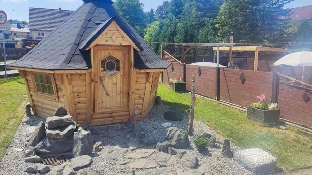 Una baita di legno con una porta esagonale e un camino, immersa tra rocce e ghiaia.